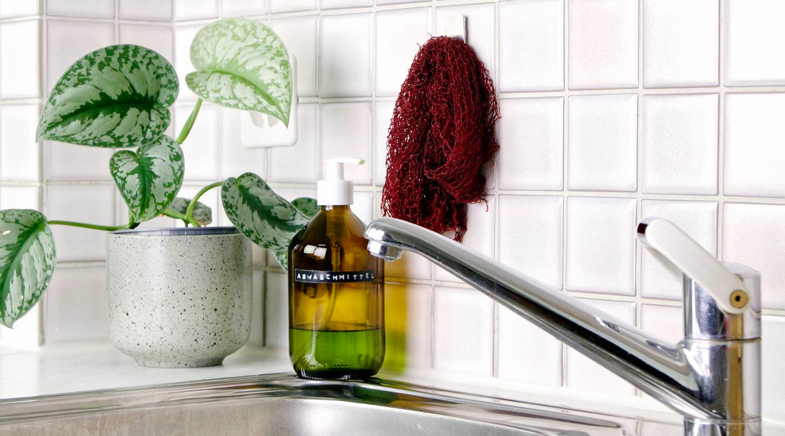 Fischnetz Spülschwamm Alternative in der Küche. Das Netz hängt an der Wand über einer Spüle mit Wasserhahn.