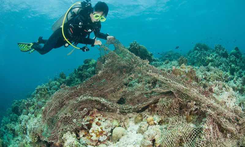 A diver picking up a discarded fishing net, also known as ghost net.