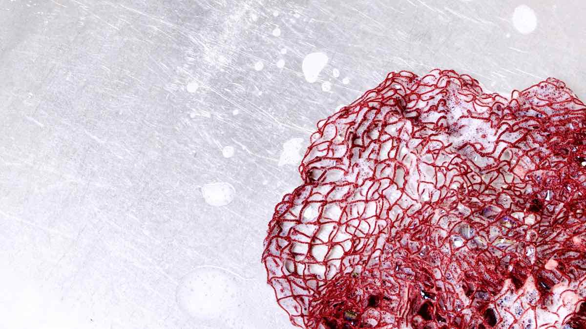 Rotes Fischnetz als Spülschwamm Alternative. Das Netz ist nass und schaumig und liegt in einem metallen Becken. Es eignet sich als ideals Einweihungsgeschenk.