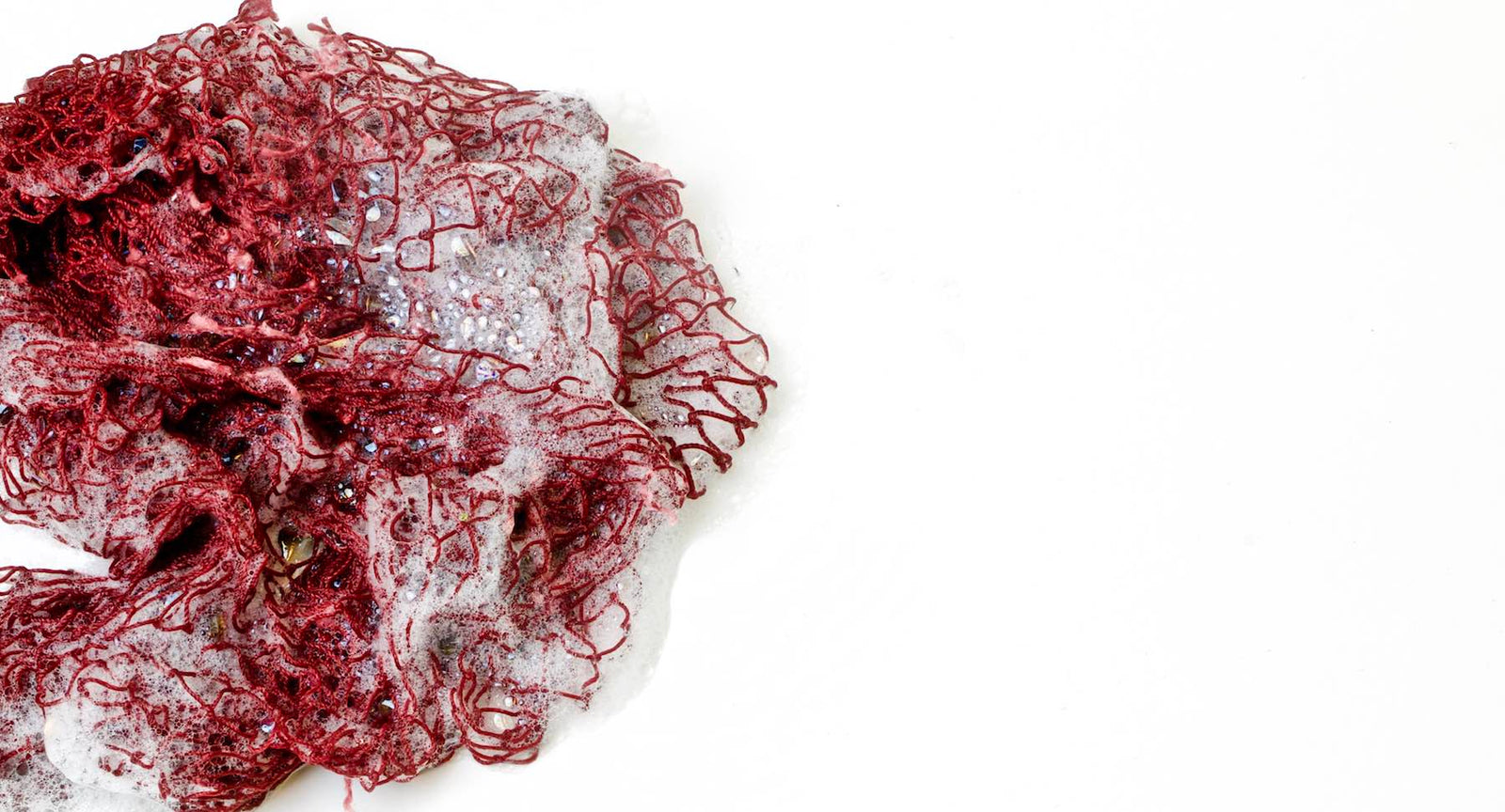 Red Fischnetz with benefits as a dish sponge alternative. The net is wet and has foam on it.