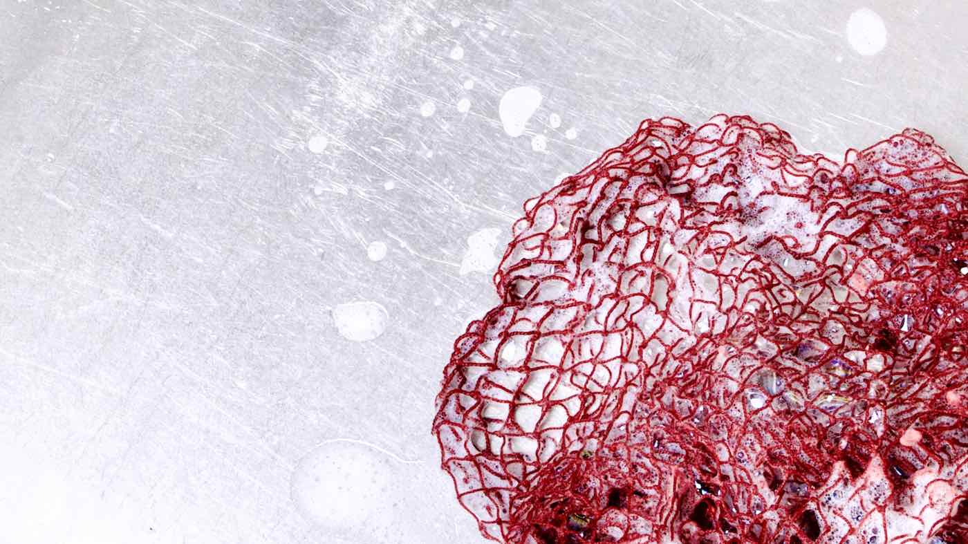 Fischnetz With Benefits as an antibacterial sponge for dishes kitchen sponge alternative. The red net is wet and has foam on it. It is lying in a kitchen sink.